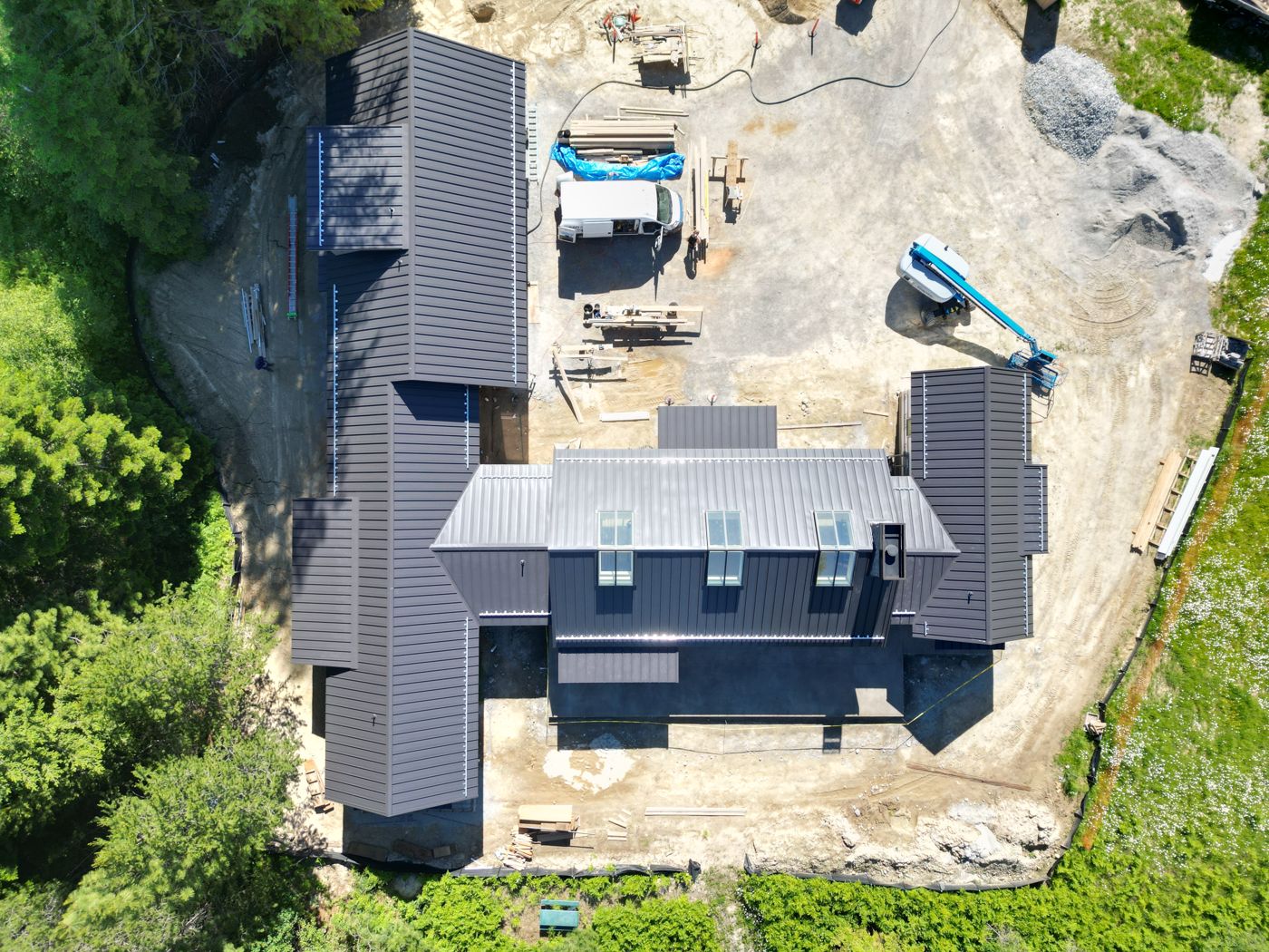 Bird's-eye drone view of dark standing seam metal roofs on a large home
