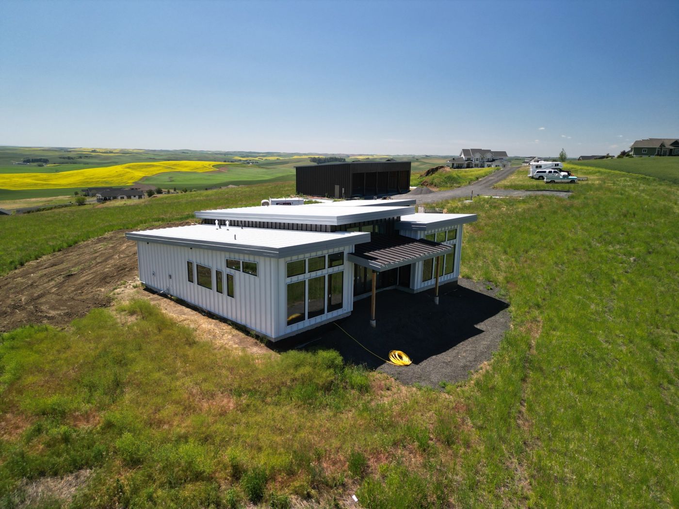 Drone view of a modern home with white low-slope metal roofs and matching white vertical metal siding in rolling farmland