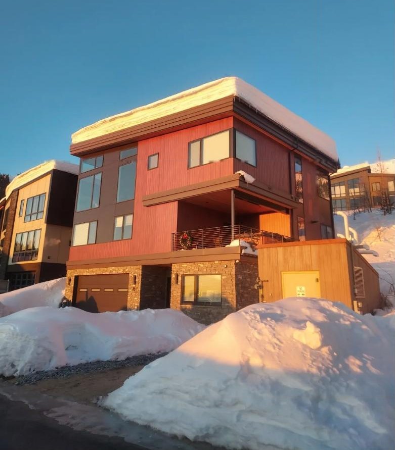 Modern three-story home with its roof covered in a thick layer of snow at sunset